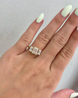A yellow gold ring featuring a large rectangular emerald-cut diamond and baguette diamond ring in a prong setting, shown on a hand