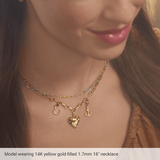 Close-up of a model wearing a delicate 14K yellow gold necklace with a multi-strand chain design, featuring a dangling heart charm, anchor charm, and small colorful bead accents.