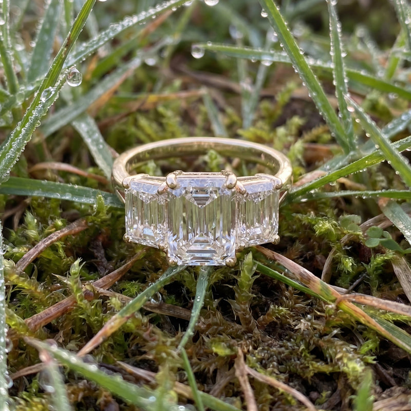 Gold ring with 3 emerald-cut diamonds on grass
