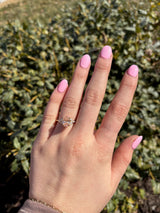 Hand with pink nail polish wearing a pink diamond ring against a green leafy background