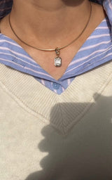 Necklace with a pendant worn by a person wearing a light-colored sweater and blue striped shirt.