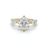 Gold ring with oval diamond center and small white diamond down sides on a white background