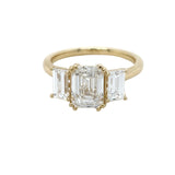 A yellow gold ring featuring a large rectangular emerald-cut diamond and baguette diamond ring in a prong setting, shown on a plain white background.